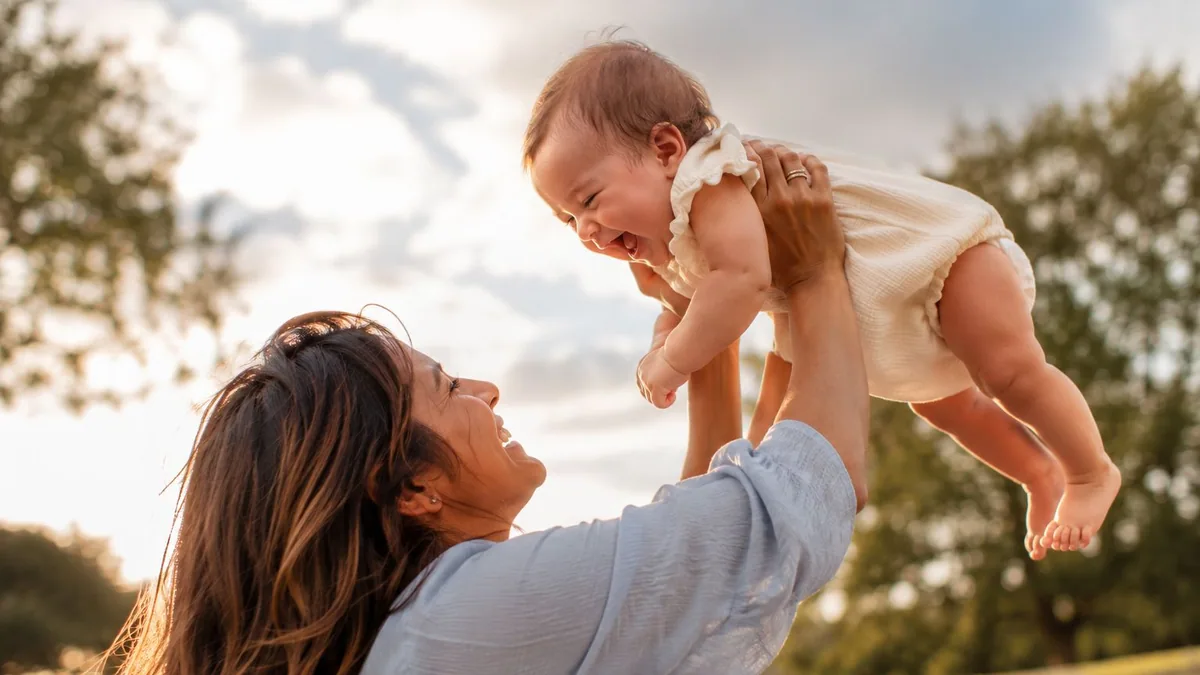 Mãe erguendo o bebê que sorri, ao ar livre no fim da tarde